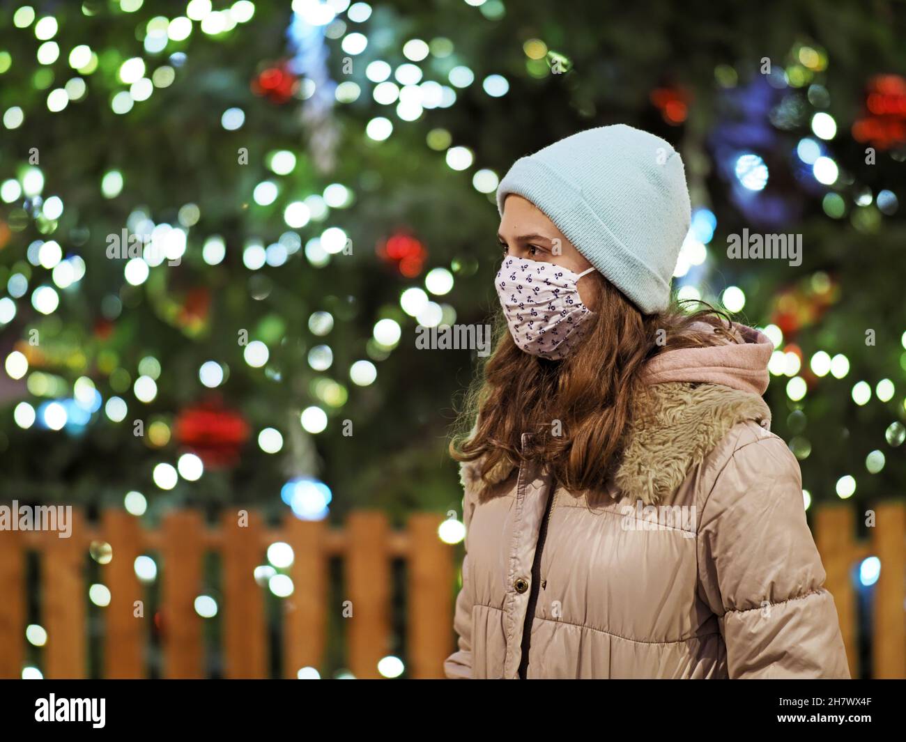 Authentisches Tenage-Mädchen vor einem Weihnachtsbaum mit Covid-Maske Stockfoto