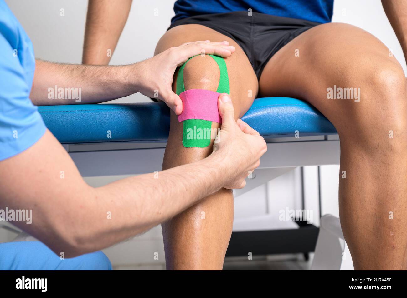 Physiotherapeut, der Kinesioband auf das Knie des männlichen Patienten aufklebt. Kinesiologie, Physiotherapie, Rehabilitationskonzept. Nahaufnahme. Hochwertige Fotos Stockfoto