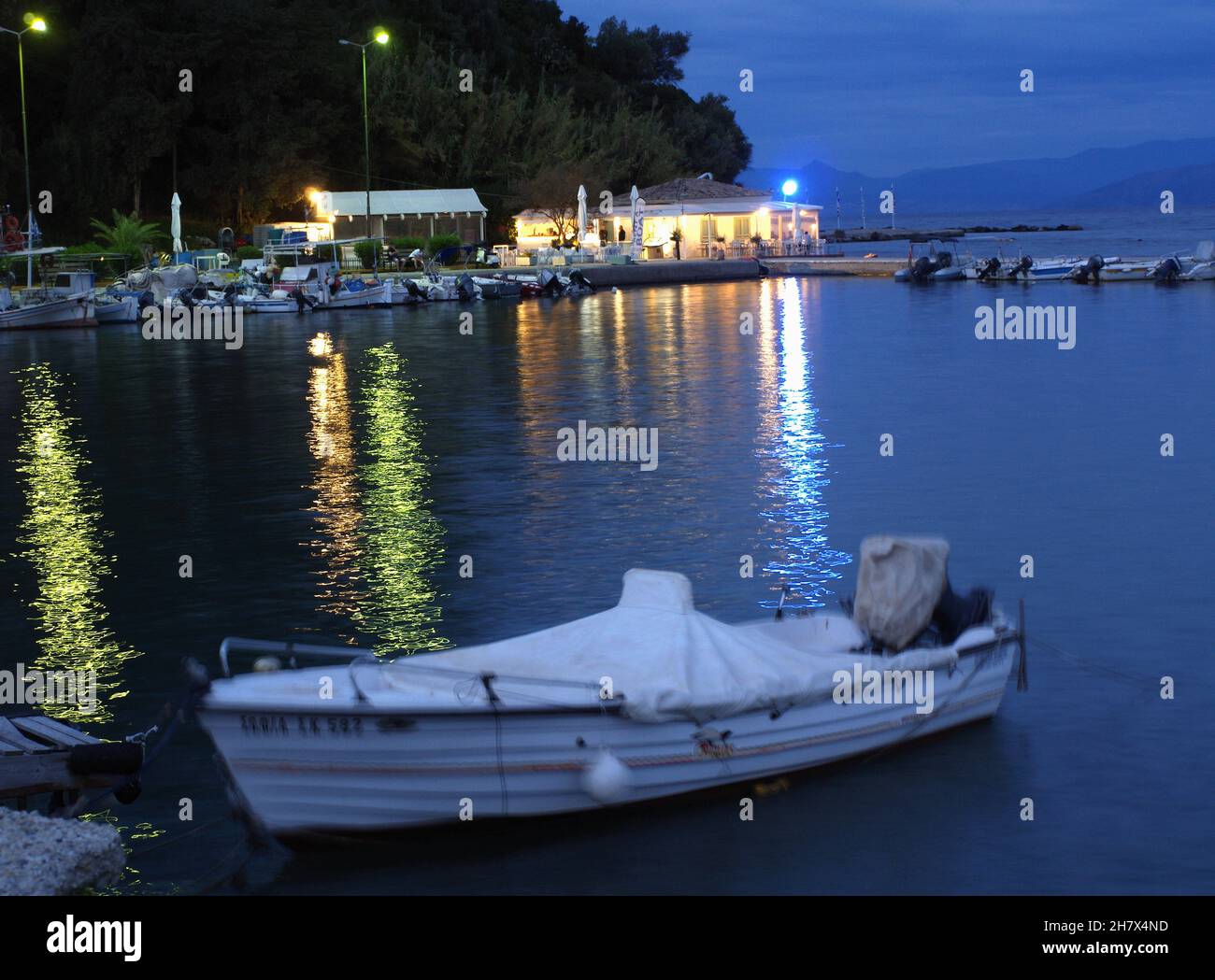 Abend in Kanoni, ein kleines Boot im Hafen mit Blick auf Flisvos Cafe und Taverna, Mouse Island, Pontikonissi, Korfu, Griechenland Stockfoto