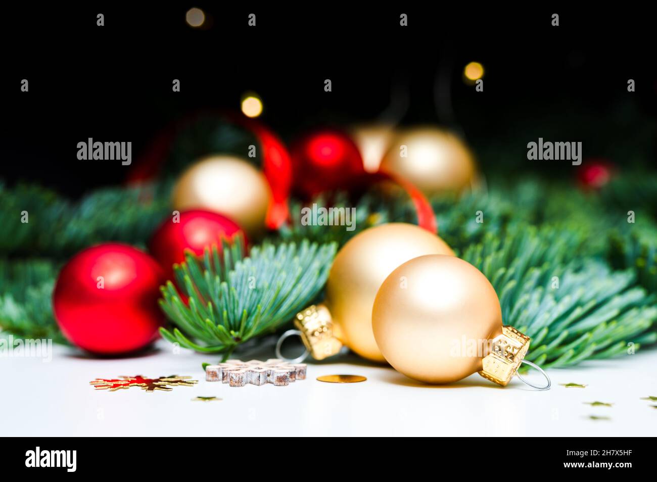 Dekoration für Weihnachtsferien. Goldene und rot schimmernde Weihnachtskugeln, Tannengrün, Konfetti-Sterne und Weihnachtslichter auf weißem Hintergrund. Stockfoto