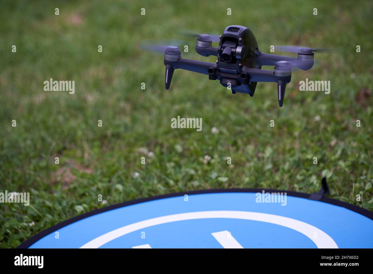 Nürtingen, Deutschland - 26. Juni 2021: Schwarze fpv-Drohne der firma dji ist zur Landung bereit. UAS mit 4 dunklen Propellern. Blauer Landeplatz und grün Stockfoto