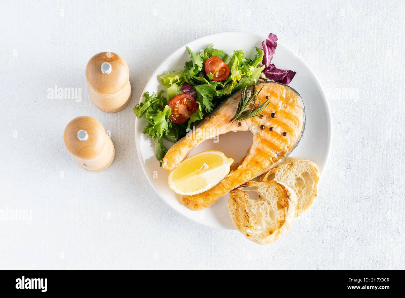 Gegrilltes Lachsfischsteak mit Salat und Tomaten auf einer weißen Keramikplatte Stockfoto