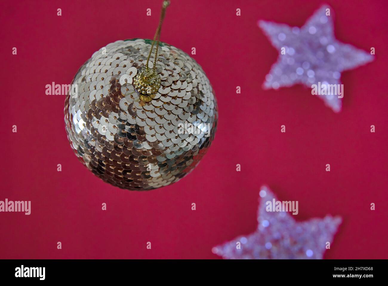 Goldener glitzernder Weihnachtsball, der auf rotem Hintergrund und glänzenden Sternen hängt. Horizontal Stockfoto