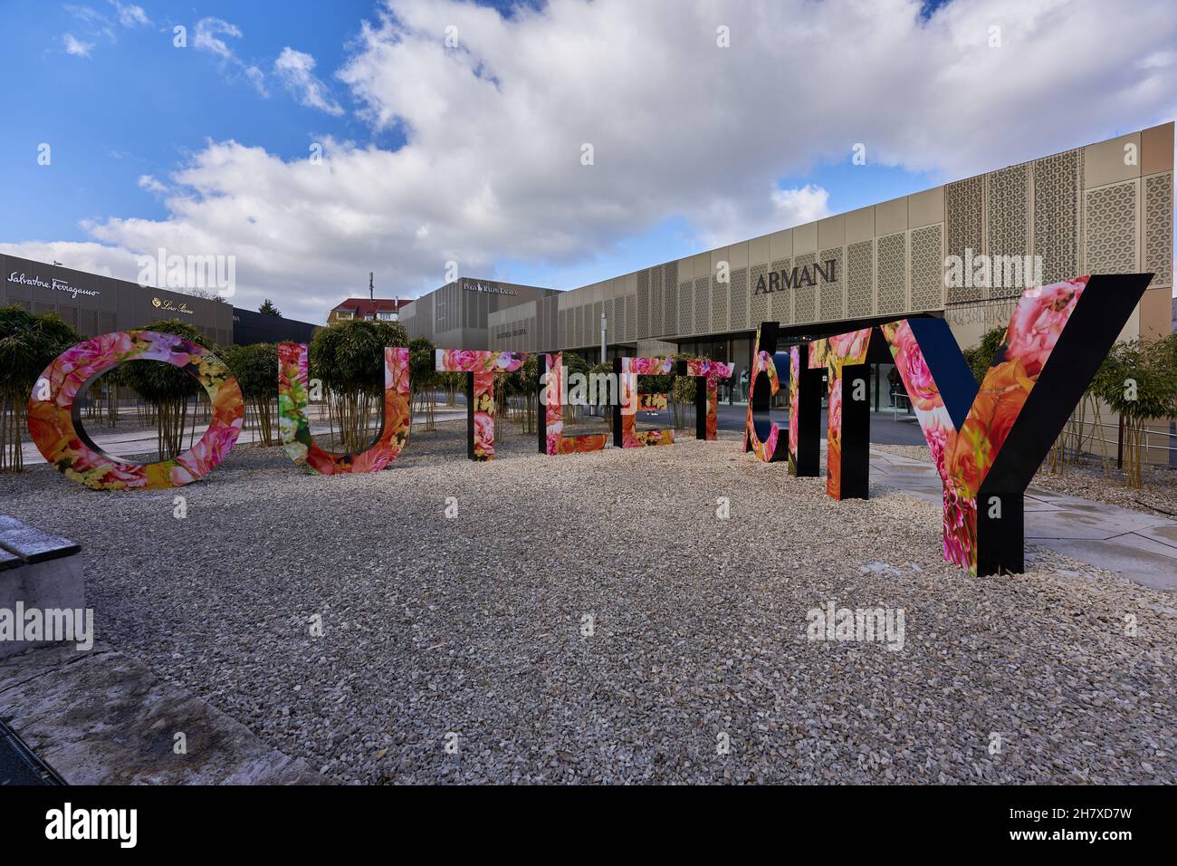 Metzingen, Deutschland - 20. März 2021: Outlet City, große bunte Buchstaben mit Blumenmuster stehen auf Kiesboden. Armani Gebäude im Hintergrund. Stockfoto