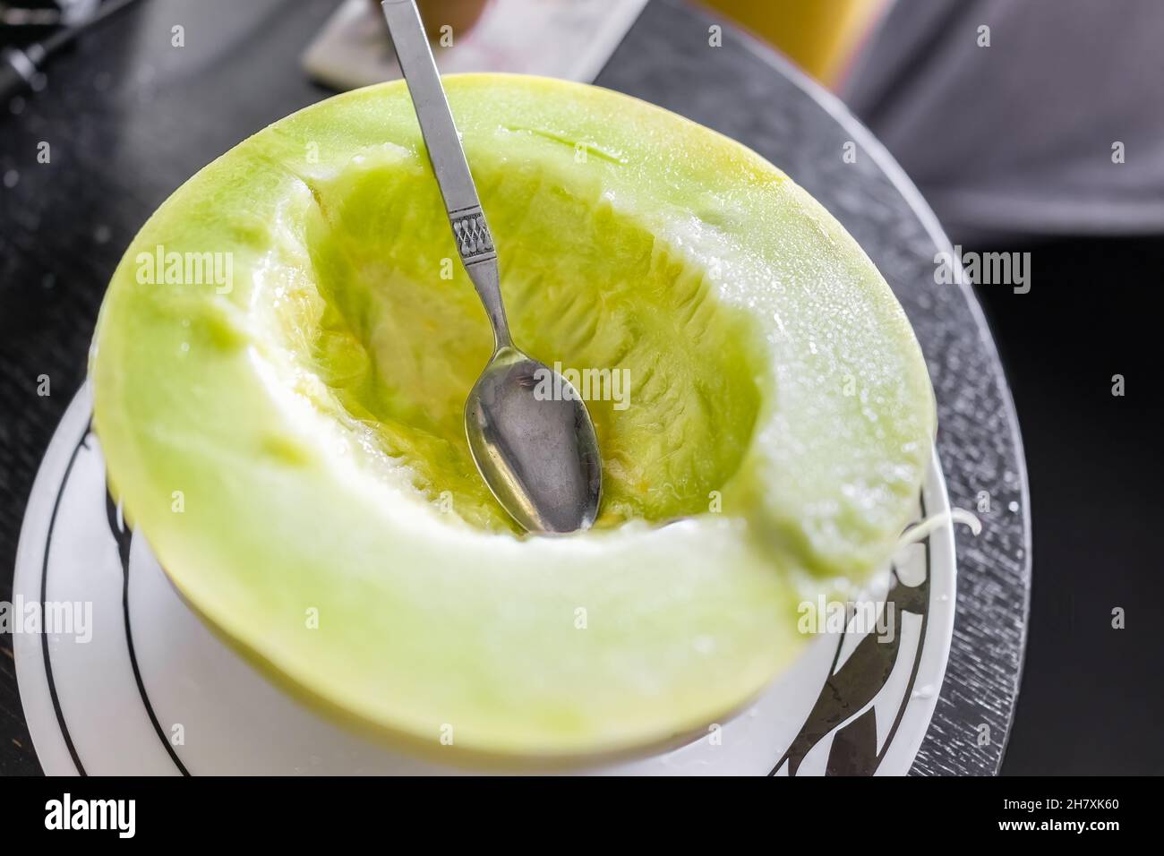 Nahaufnahme einer leuchtend bunten, gelb-grünen Honigmelone, halb geschnitten, mit Löffel, der auf dem Teller isst Stockfoto