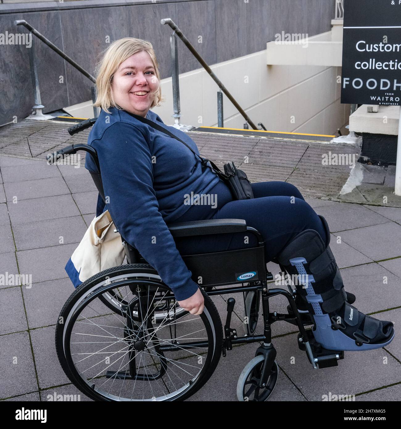 Junge Dame in einem Rollstuhl und Luftstiefel, nachdem sie an zwei Stellen einen gebrochenen Fuß erlitten hatte Stockfoto