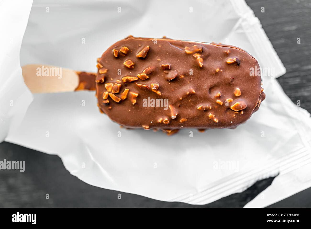 Makro-Nahaufnahme flach Lay Draufsicht von einer Schokolade Mandelnüsse Eis Bar auf Holzstock mit Kunststoff weiß Wrap Verpackung auf Küchentisch Stockfoto