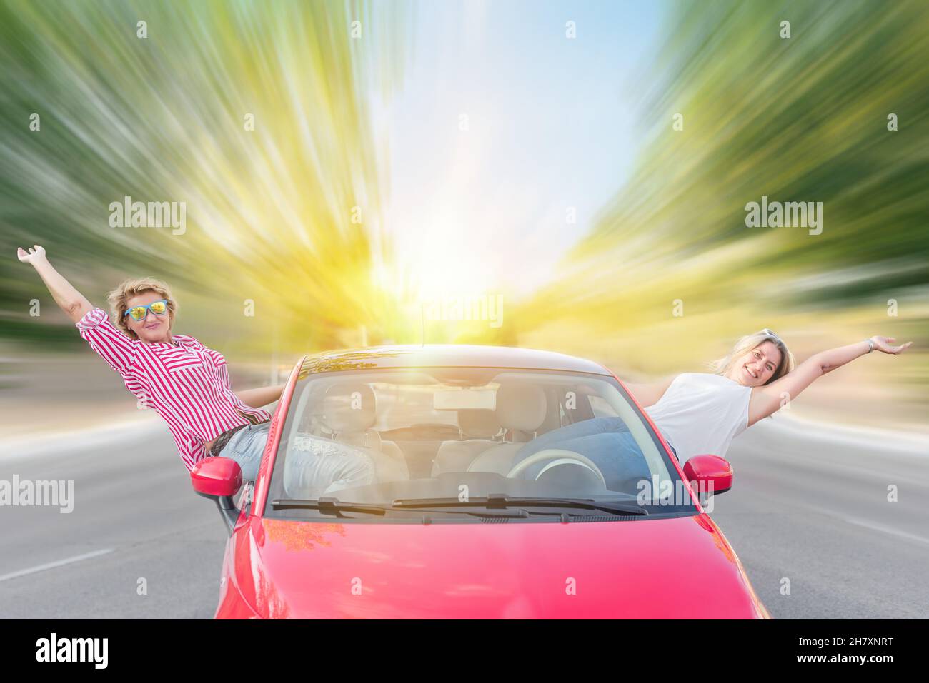 Zwei wilde und verrückte kaukasische Frauen mit ihrem Mietwagen auf der Autobahn sitzen in den Türen und stecken ihre Körper aus dem Fahrzeug. Thelma und Loui Stockfoto