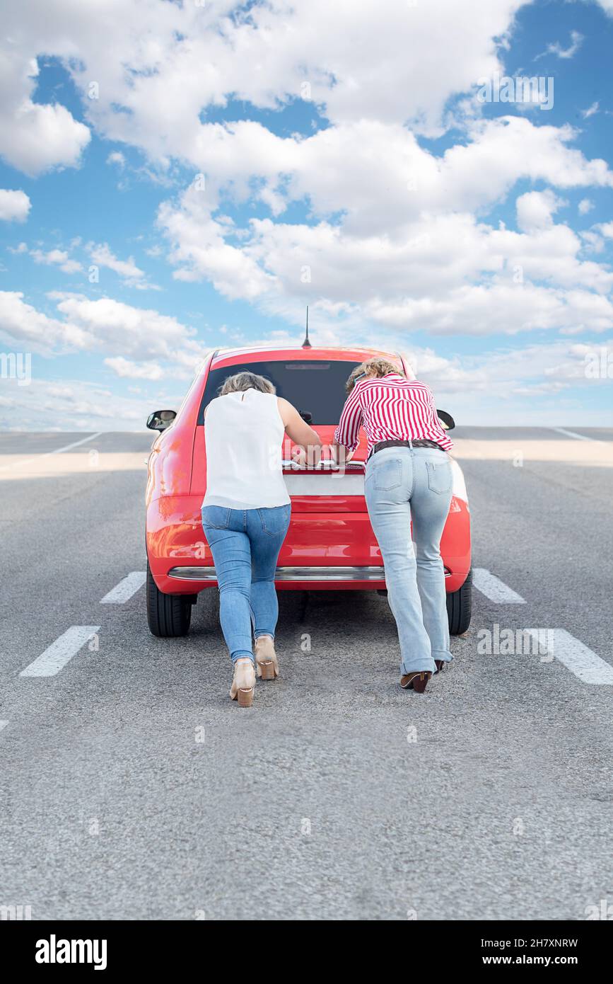 Zwei weibliche Touristen schieben einen roten Mietwagen, nachdem er wegen eines Pannenausfalls in der Mitte der Autobahn steht Stockfoto