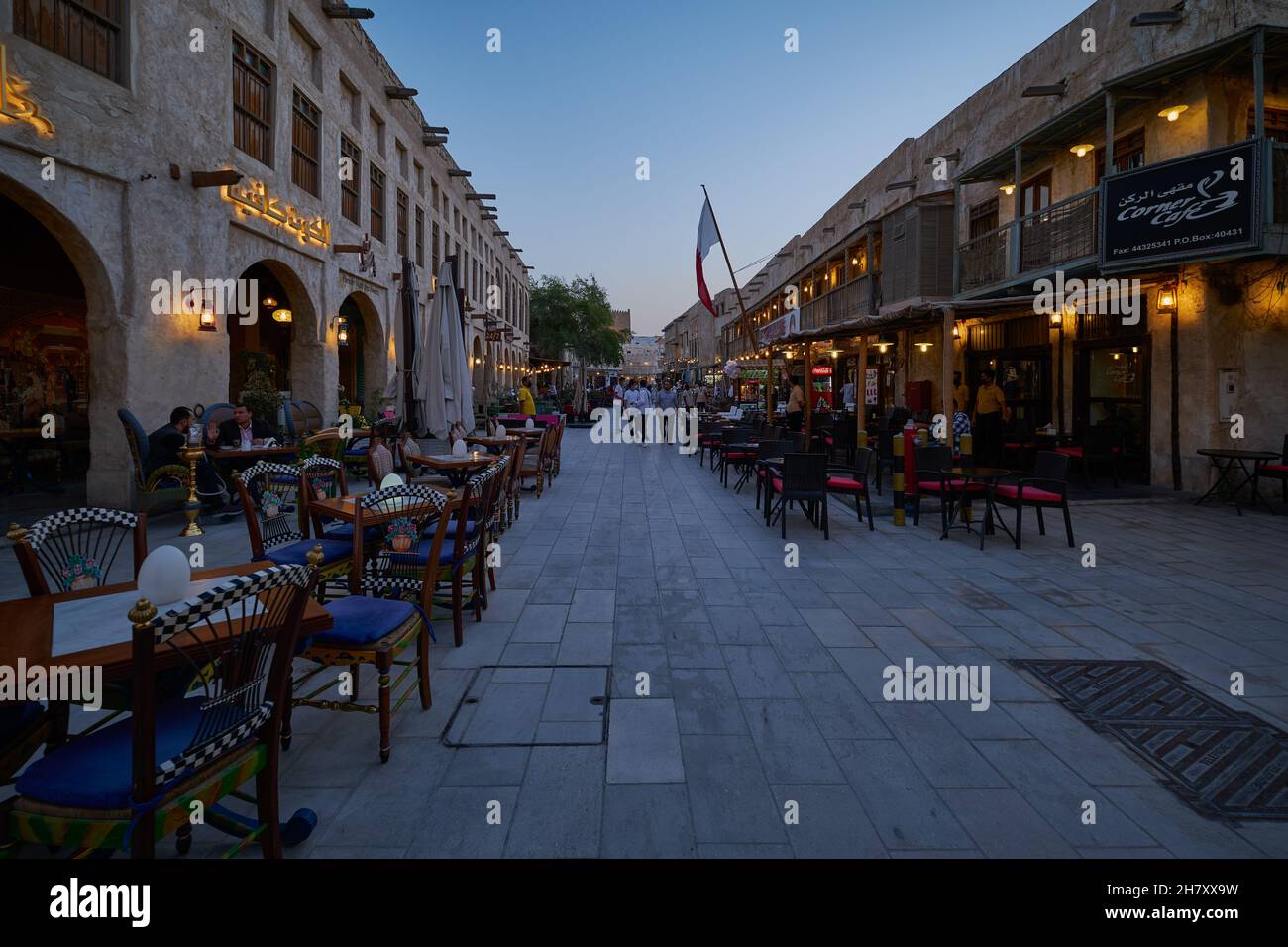 Souq Waqif Doha, Katar Tageslichtansicht mit Hauptstraße mit Café, Restaurants, Menschen zu Fuß und Qatar Flagge Stockfoto