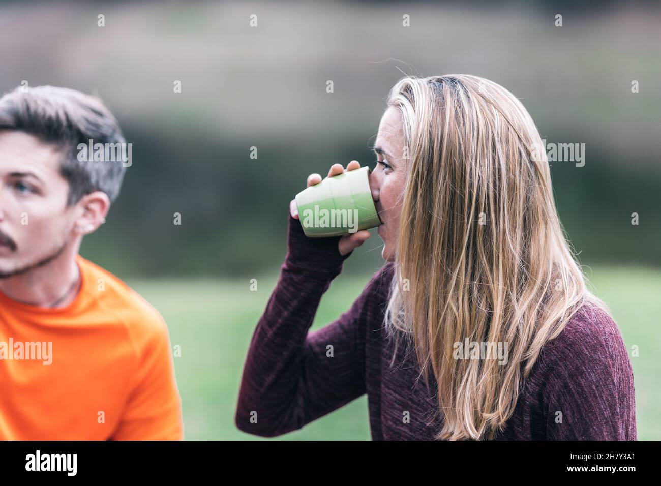 Blonde, fit Frau trinkt Tee in einem Park neben anderen Menschen Stockfoto