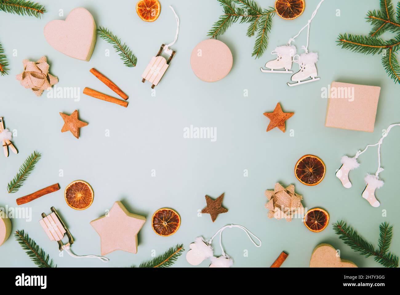 Draufsicht Weihnachtsrahmen aus Tannenzweigen, umweltfreundliche Pappschachteln, Holzspielzeug, Zimt, getrocknete Orangen auf hellgrünem Hintergrund. Null-wast Stockfoto