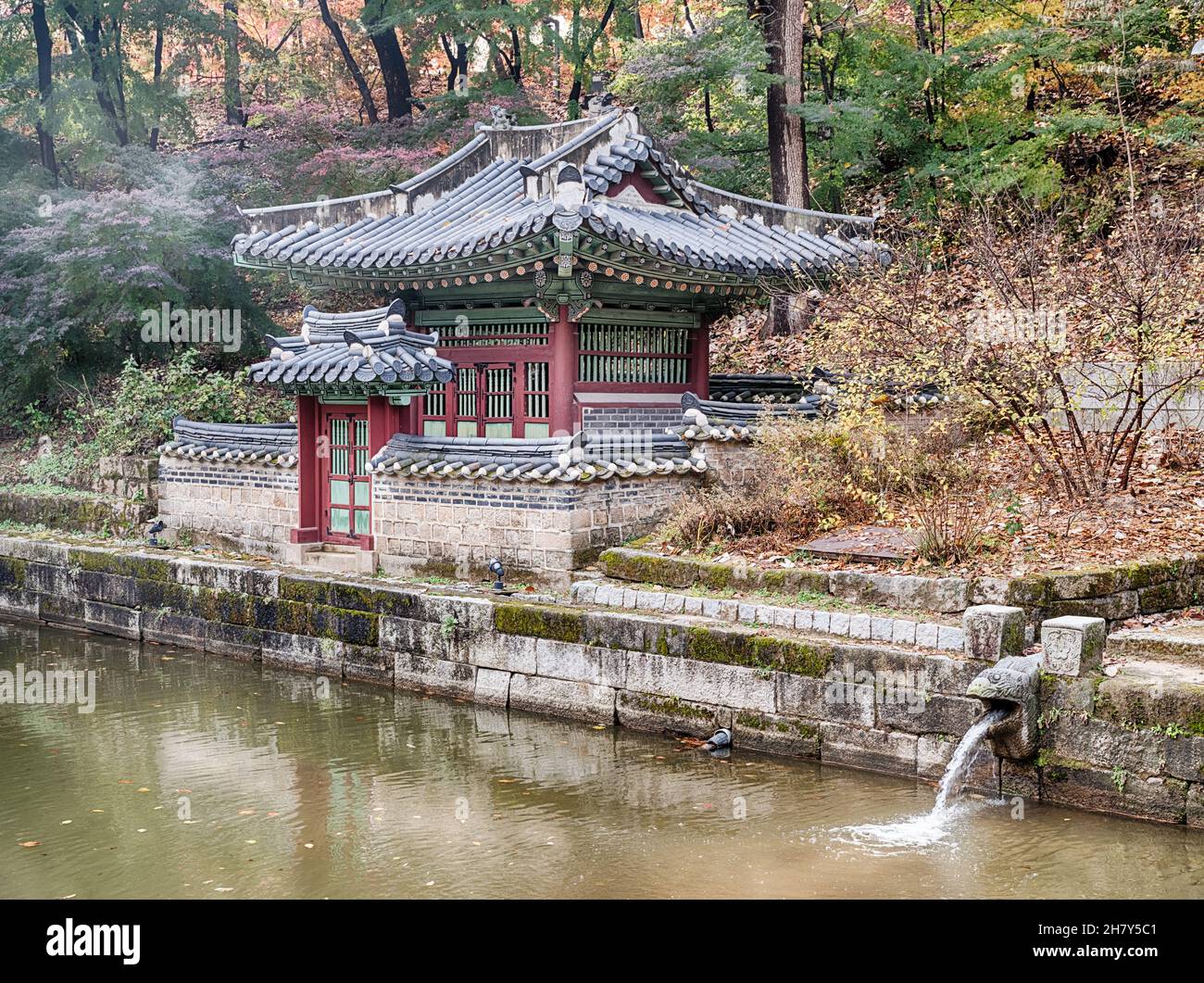 Eine kleine Villa liegt an einem Teich, während ein kleiner Bach ins Wasser fließt. Stockfoto