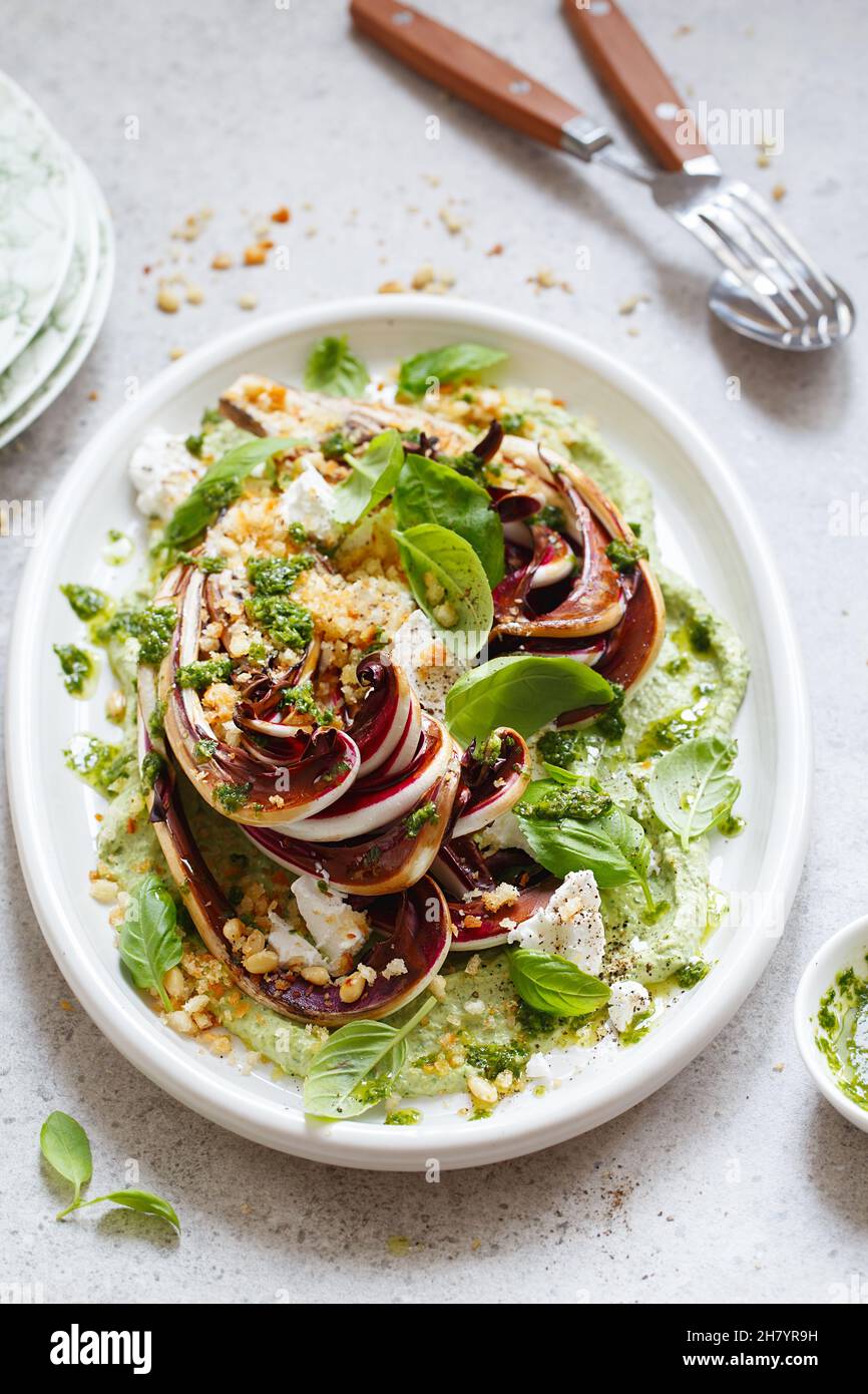 Gerösteter Radicchio-Salat mit Feta, grünem Tahini, Pinienkernen und Basilikum-Pesto. Radicchio rosso di treviso tardivo, italienischer roter Chicorée. Gesunde Mahlzeit reci Stockfoto