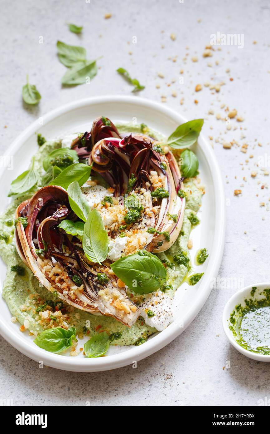 Gerösteter Radicchio-Salat mit Feta, grünem Tahini, Pinienkernen und Basilikum-Pesto. Radicchio rosso di treviso tardivo, italienischer roter Chicorée. Gesunde Mahlzeit reci Stockfoto