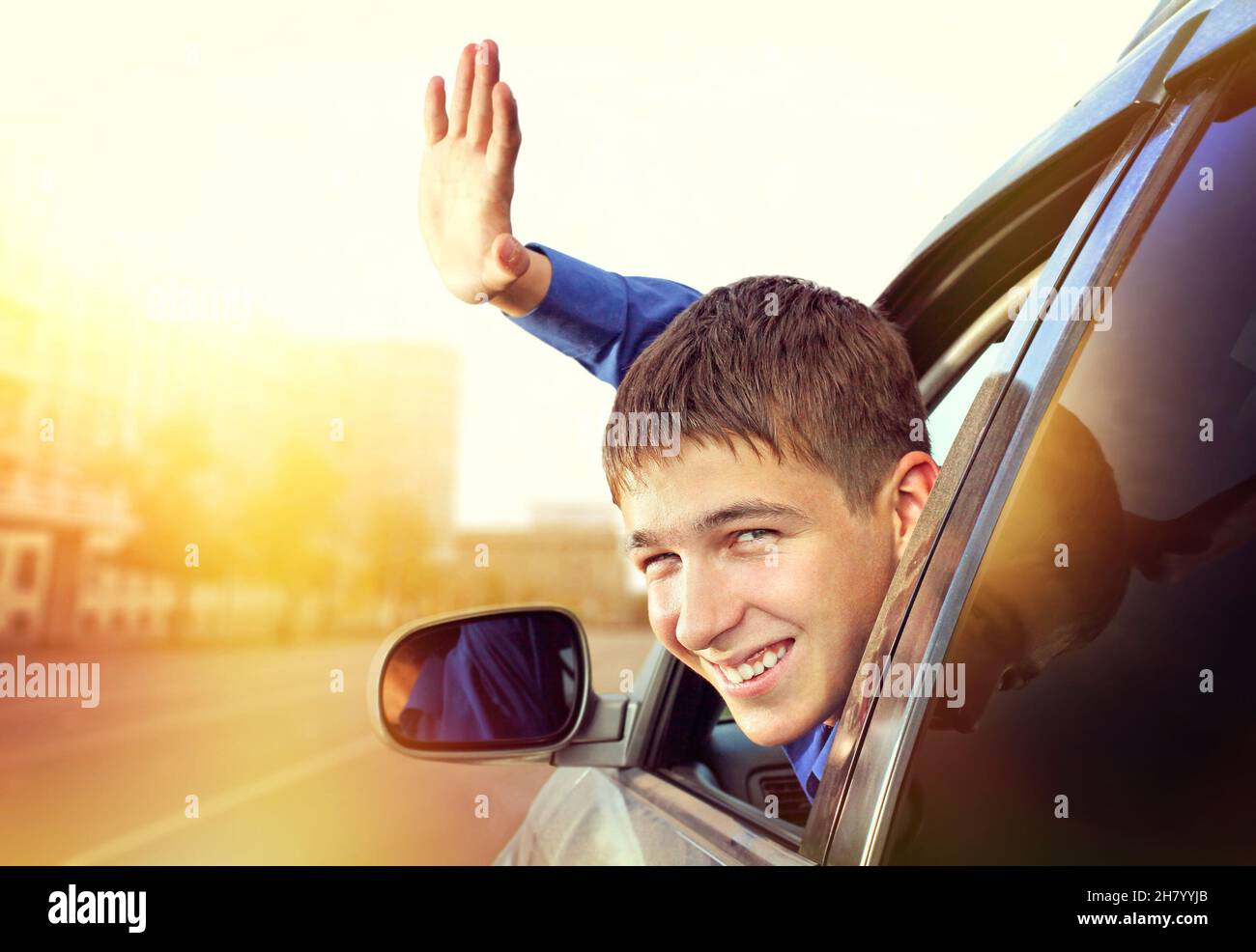 Fröhlicher junger Mann sitzt im Auto auf der City Street Stockfoto