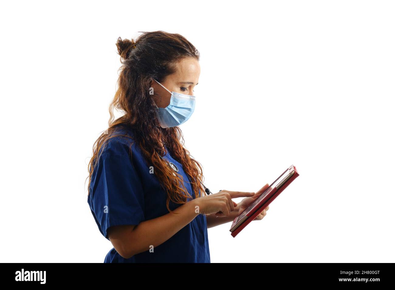 Ärztin in einer Gesichtsmaske und OP-Uniform mit einer digitalen Tablette, während sie auf einem isolierten Hintergrund steht. Stockfoto