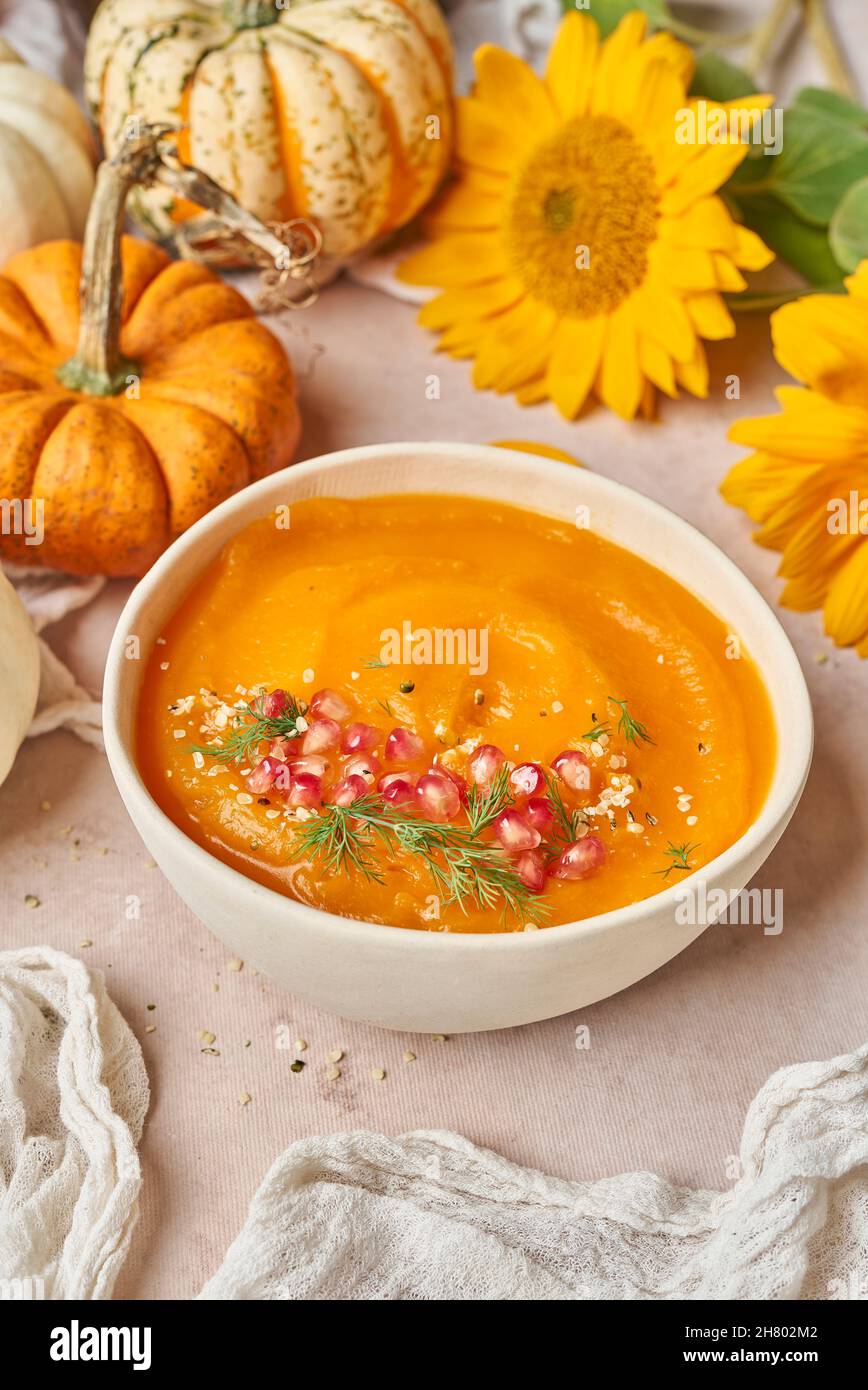 Schüssel mit leckeren Kürbissuppe mit Granatapfelkernen verziert auf den Tisch mit Gemüse und gelben Sonnenblumen in der Küche gelegt Stockfoto