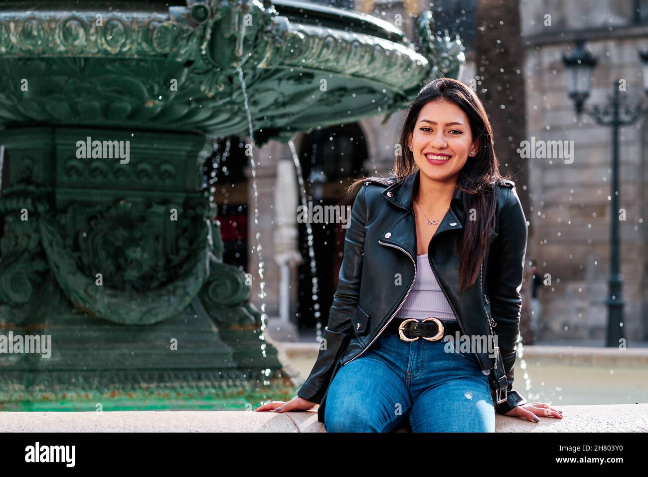 Frau lächelt, während sie draußen auf einem Springbrunnen sitzt. Stockfoto