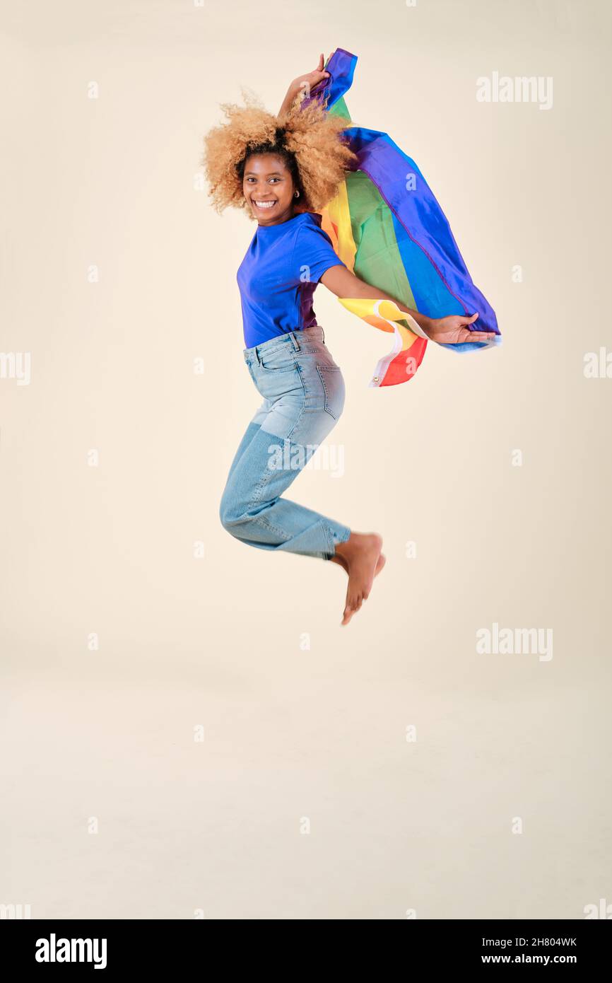 Fröhliche und aufgeregte Affronin, die mit einer lgbt-Stolzflagge in Regenbogenfarben springt. Stockfoto