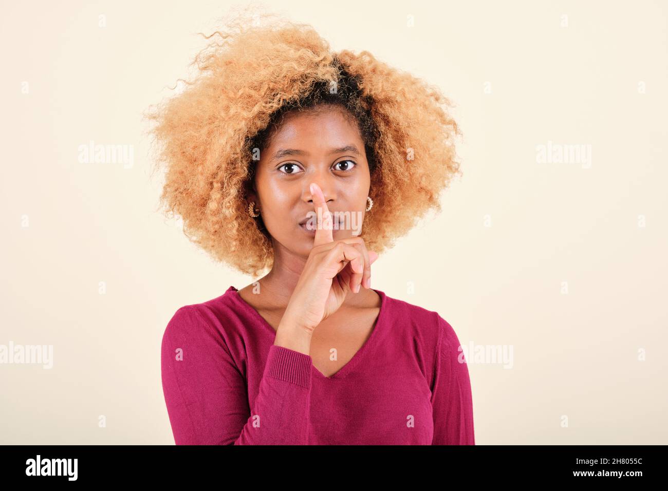 Afro-Frau, die den Finger in den Mund legt, während sie auf einem isolierten Hintergrund eine stille Geste macht. Stockfoto