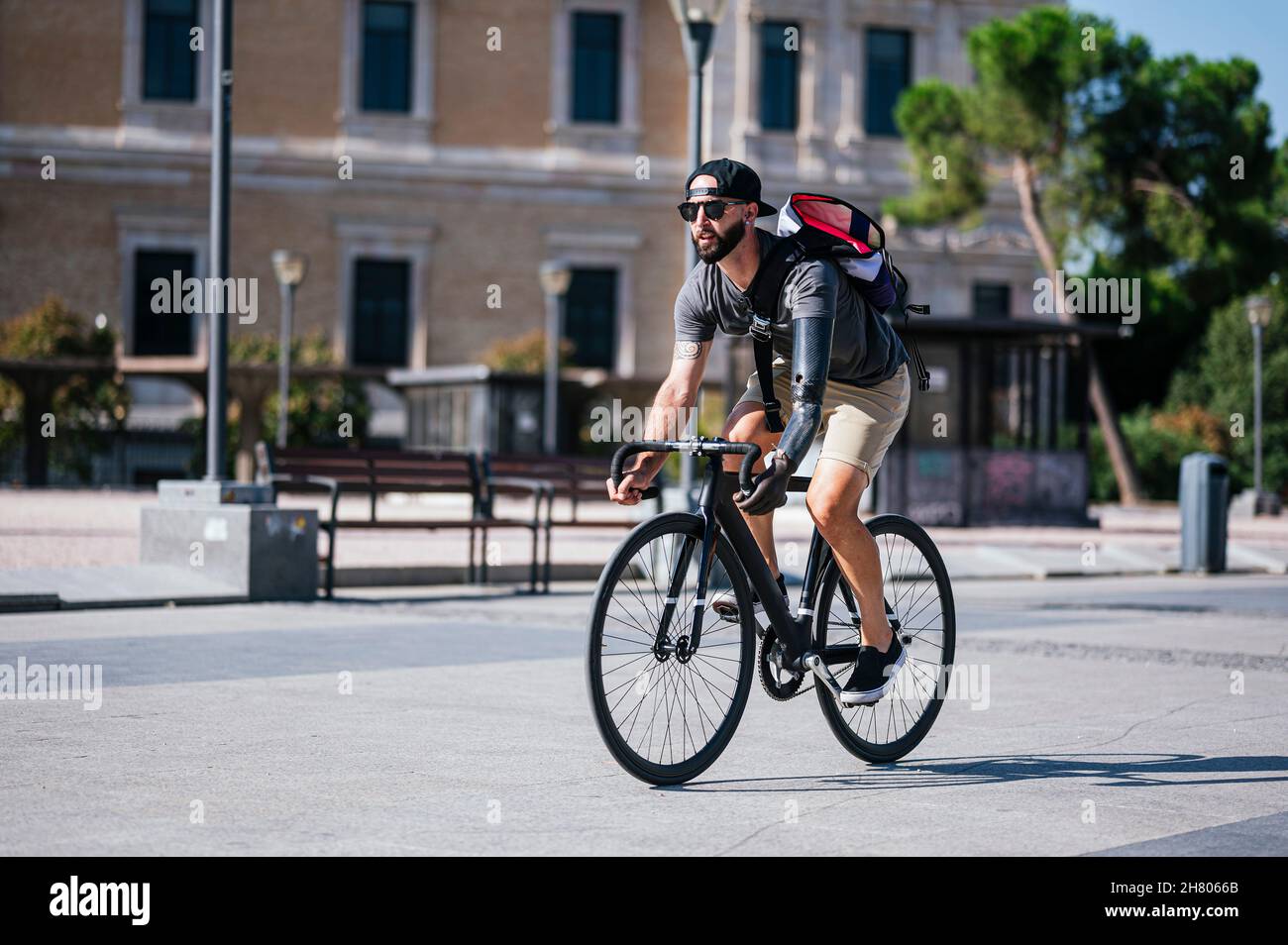 Bärtiger Hipster mit künstlichem Arm, der im Sommer in der Stadt Fahrrad auf der Straße reitet Stockfoto