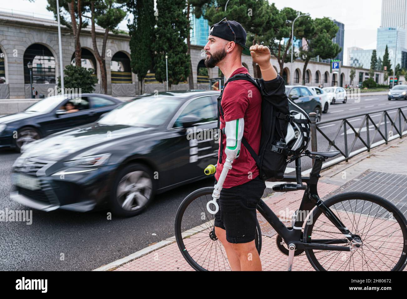 Seitenansicht eines männlichen Hipsters mit Armprothese, der mit dem Fahrrad in der Nähe des Fußgängerübergangs in der Stadt steht Stockfoto