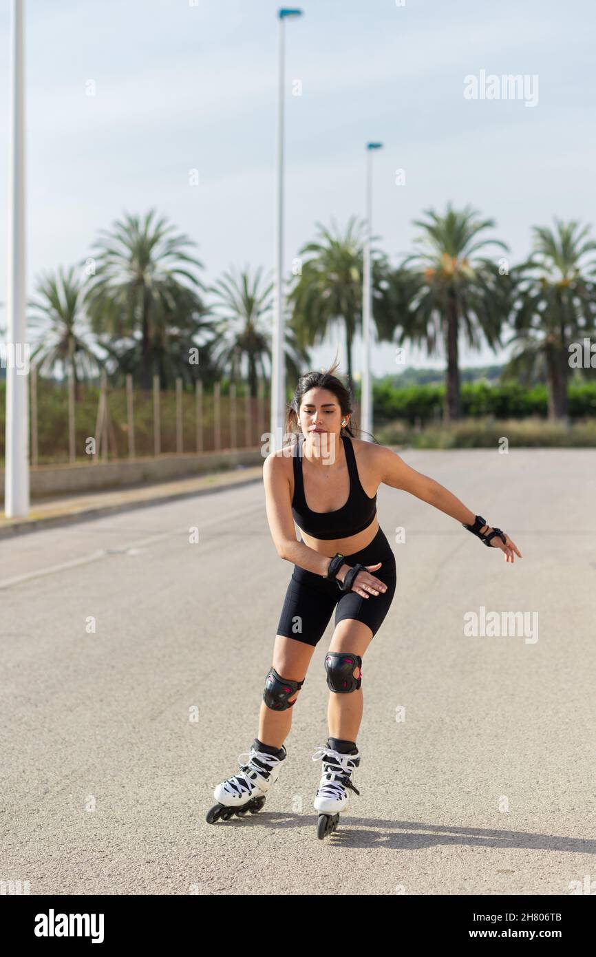 Flauschige Frau mit körperlichem Sitz im aktiven Ohr, fliegende Haare auf Rollerklingen laufen und Musik in den TWS-Ohrstöpseln hören Stockfoto