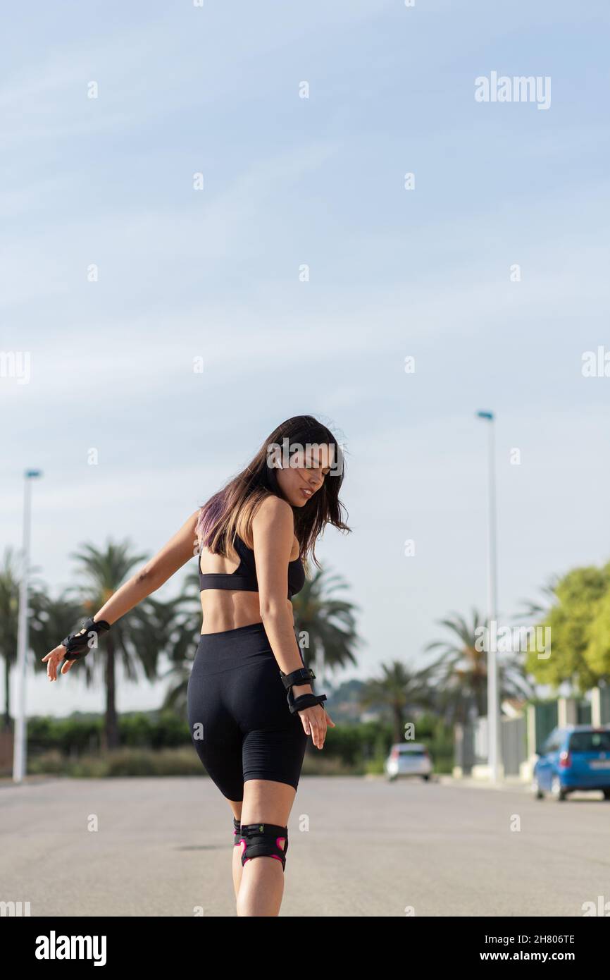 Fokussierte Passform für Frauen im aktiven Ohr mit fliegendem Haarskaten auf Rollerblades und Musikhören in TWS-Ohrhörern Stockfoto