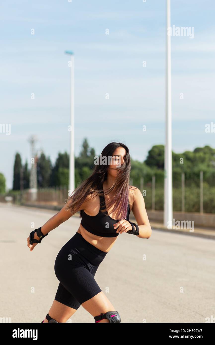 Focused fit female in Active-Ear mit fliegenden Haaren und geschlossenen Augen beim Schlittschuhlaufen auf Rollerklingen Stockfoto