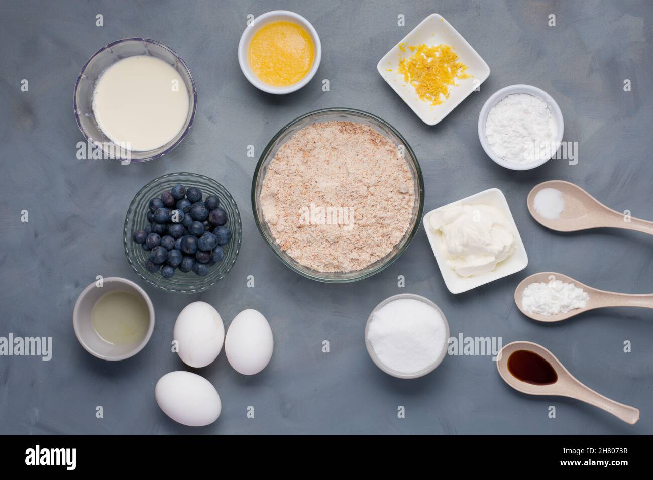 Draufsicht auf verschiedene Zutaten, darunter Milch geschmolzene Butter in der Nähe von Schalen mit Zitronenschale Mehl Zucker Salz in der Nähe von saurem Rahm Sodaöl und Heidelbeeren Eier Stockfoto