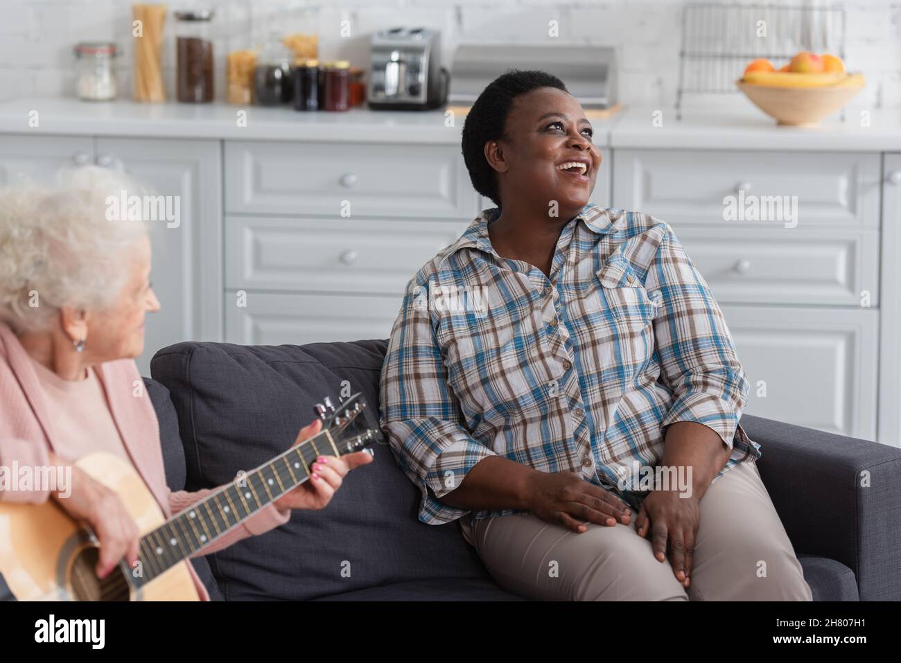 afroamerikanische Frau, die in der Nähe einer älteren Freundin singt, die im Pflegeheim akustische Gitarre spielt Stockfoto