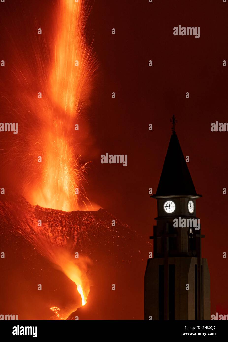 Dramatische Kulisse der Silhouette des Kirchturms am Berghang gegen den mächtigen Ausbruch des Vulkans Cumbre Vieja in der Nacht auf der Insel La Palma Stockfoto