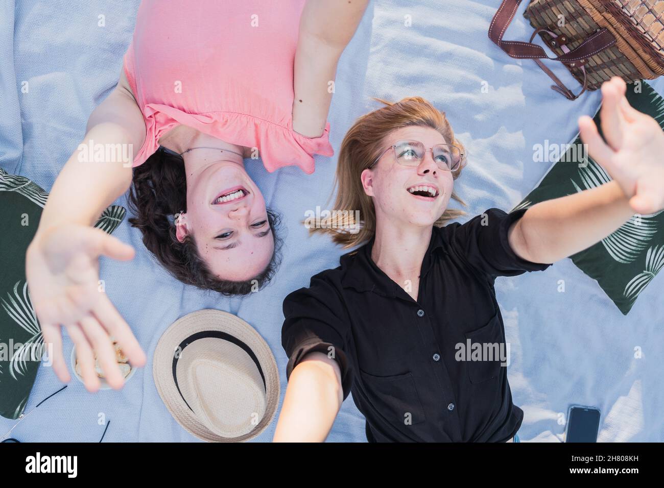 Draufsicht auf entzückende junge Freundinnen, die auf der Decke liegen und eine Kamerafunke machen, während sie sich während des Picknicks an sonnigen Tagen amüsieren Stockfoto
