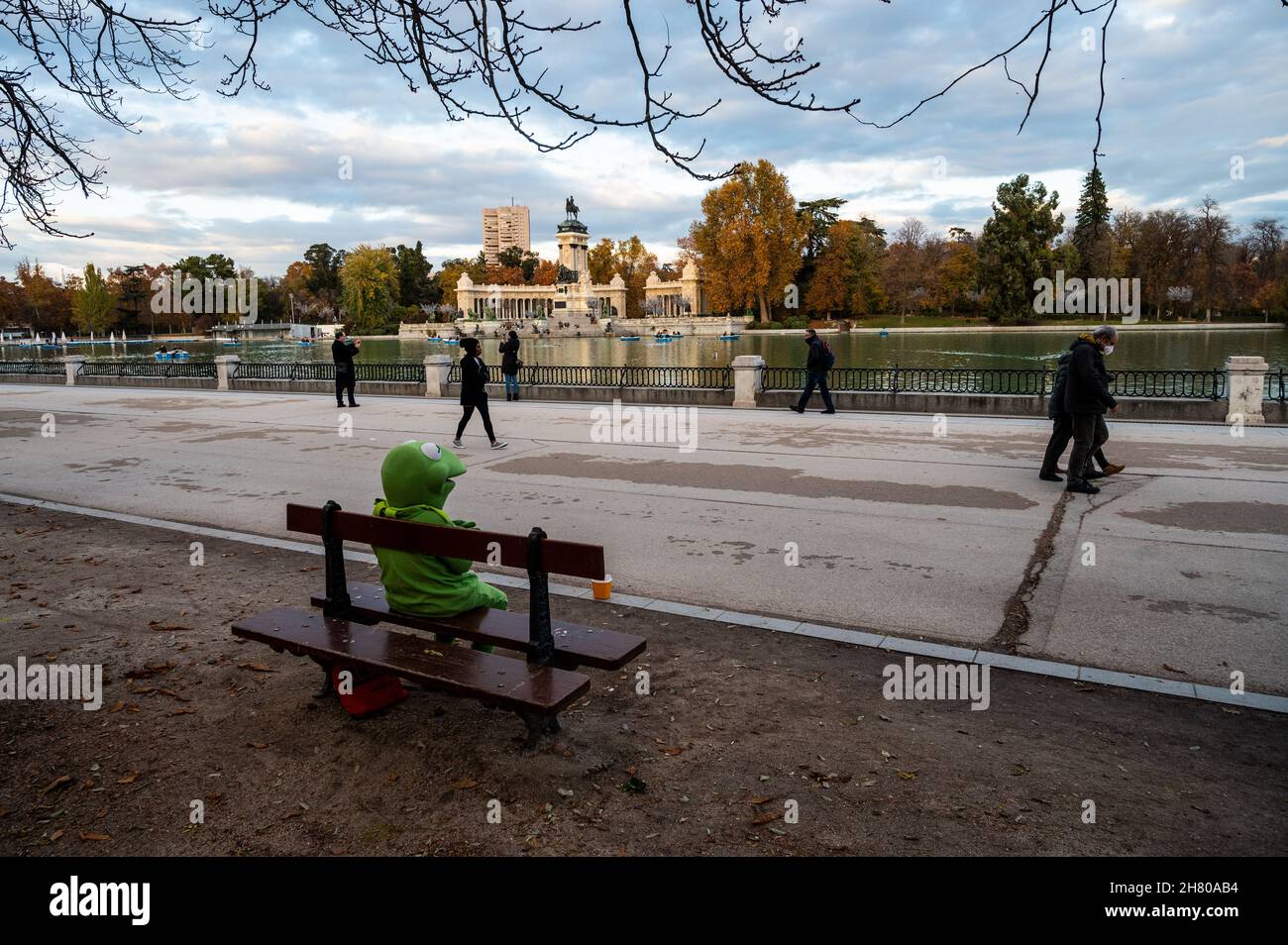 Madrid, Spanien. 25th. November 2021. Ein Mann, der als Kermit der Frosch gekleidet war, sitzt an einem Herbsttag auf einer Bank im Retiro Park und wartet darauf, einige Münzen von Besuchern zu erhalten. Quelle: Marcos del Mazo/Alamy Live News Stockfoto