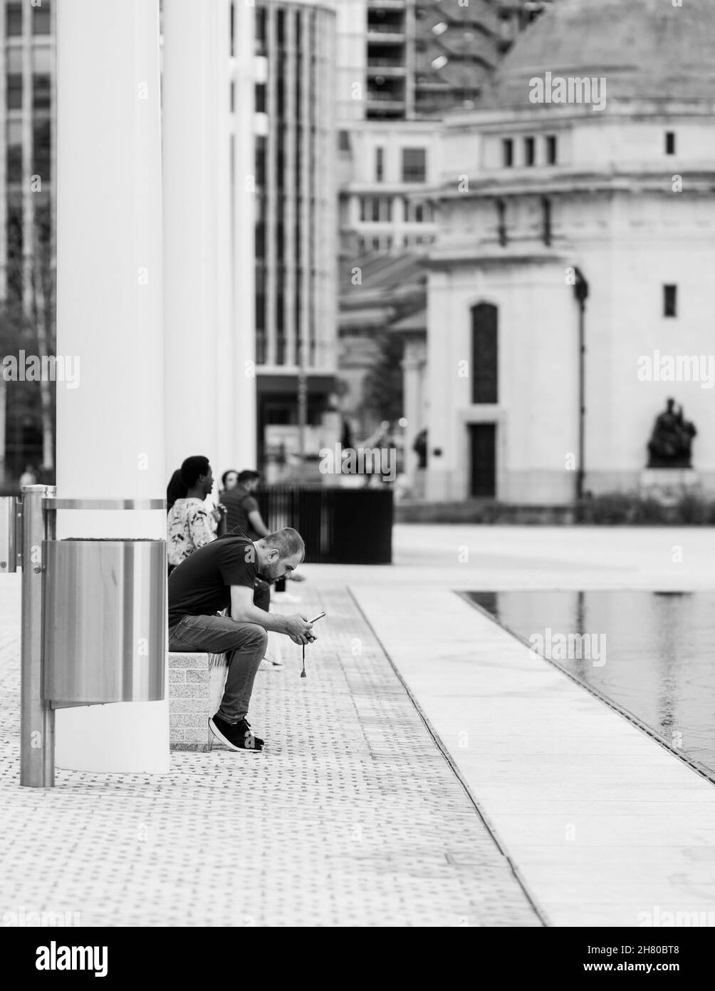 BIRMINGHAM, VEREINIGTES KÖNIGREICH - 03. Sep 2020: Eine vertikale Graustufe eines Mannes, der auf einer Bank in Birmingham im Vereinigten Königreich sitzt Stockfoto