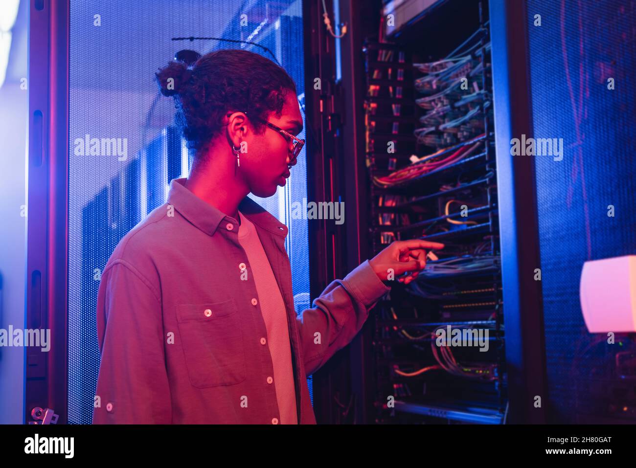 afroamerikanischer Techniker überprüft die Kabel des Servers im Rechenzentrum Stockfoto