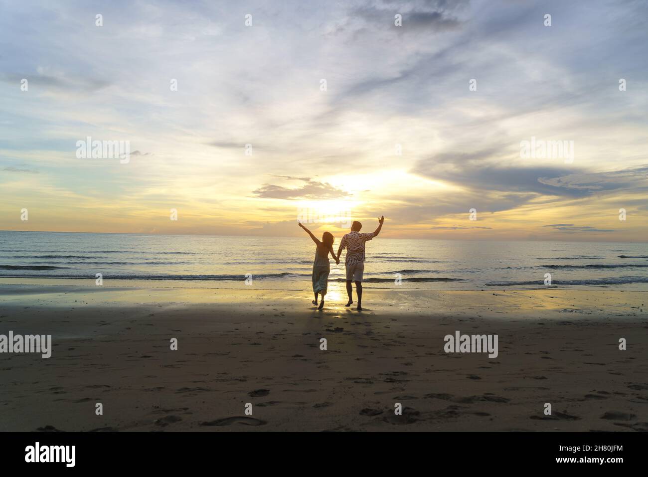 Asiatische Frau Reisende halten Mann die Hand und schauen schönen Sonnenuntergang am Strand, Paar im Urlaub im Sommer und Freiheit Konzept Stockfoto