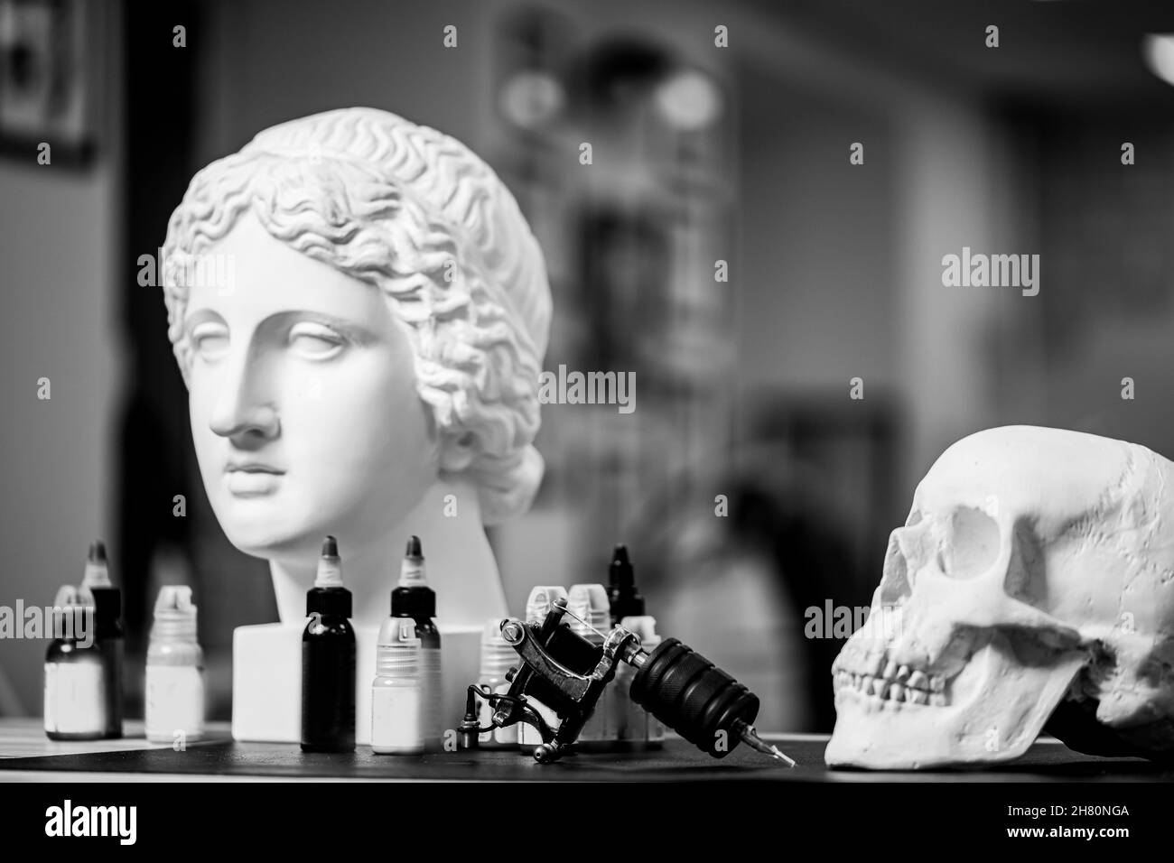 Arbeitsplatz von Tattoo-Künstler mit Tinte für Zeichnungen und antike Figuren und Totenkopf, schwarz-weiß Foto. Stockfoto