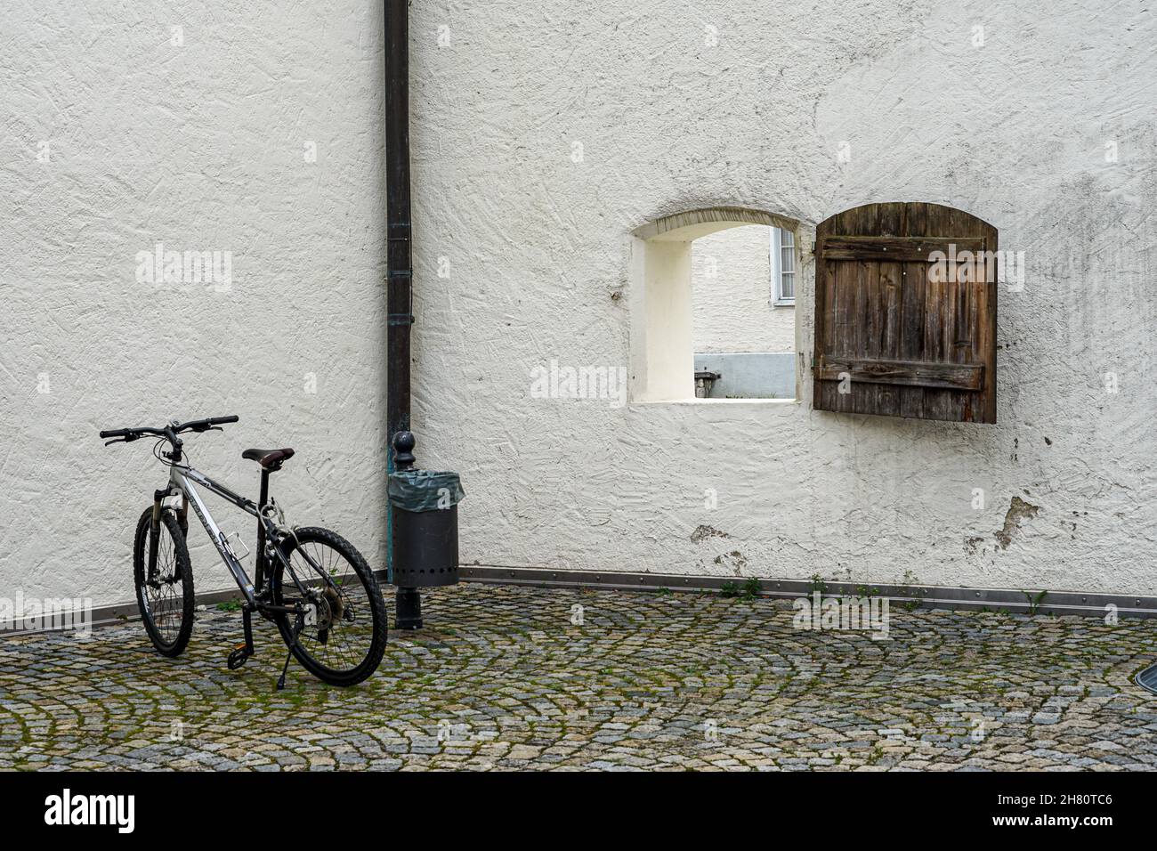 Geparktes Fahrrad in einem Innenhof vor einem Laternenpfahl mit einem Papierkorb.Blick auf die Straße durch ein Fenster, das in der Wand öffnet. Stockfoto