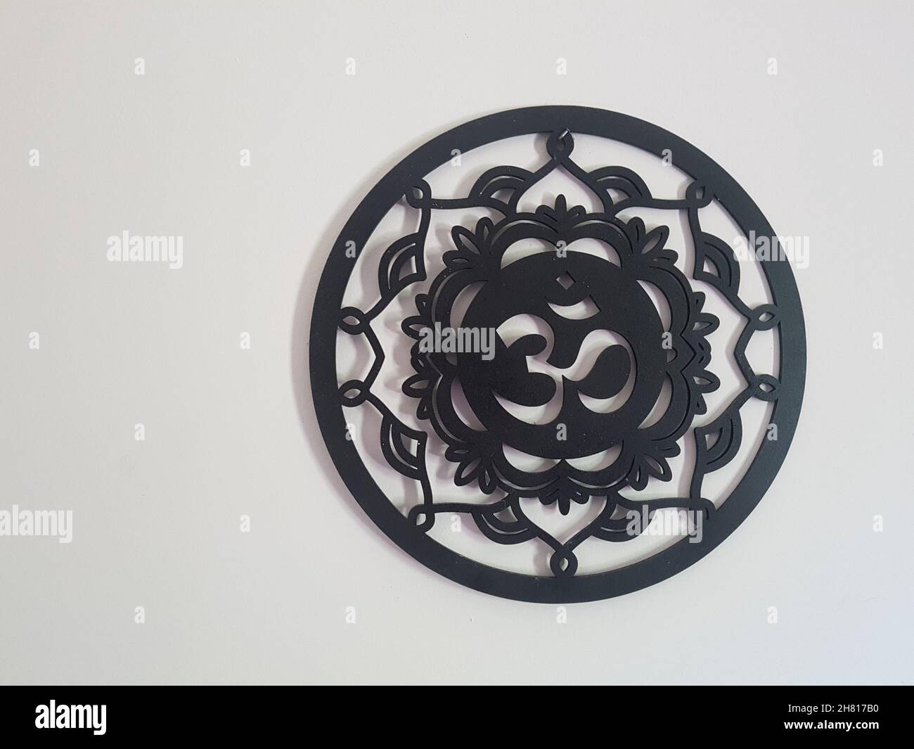 OM Symbol in einem hölzernen Mandala in schwarzer Farbe auf einer weißen Wand. Stockfoto