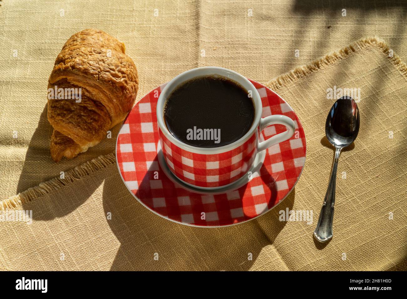 Tasse Kaffee und Croissant, vom Sonnenlicht beleuchtet, Herbsttag, Draufsicht. Stockfoto