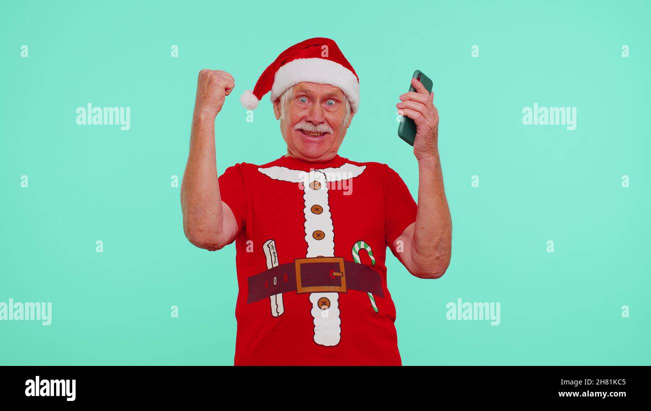 Großvater in Weihnachten T-Shirt suchen Smartphone-Display aufrichtig jubeln Erfolg Glück gewinnen Stockfoto