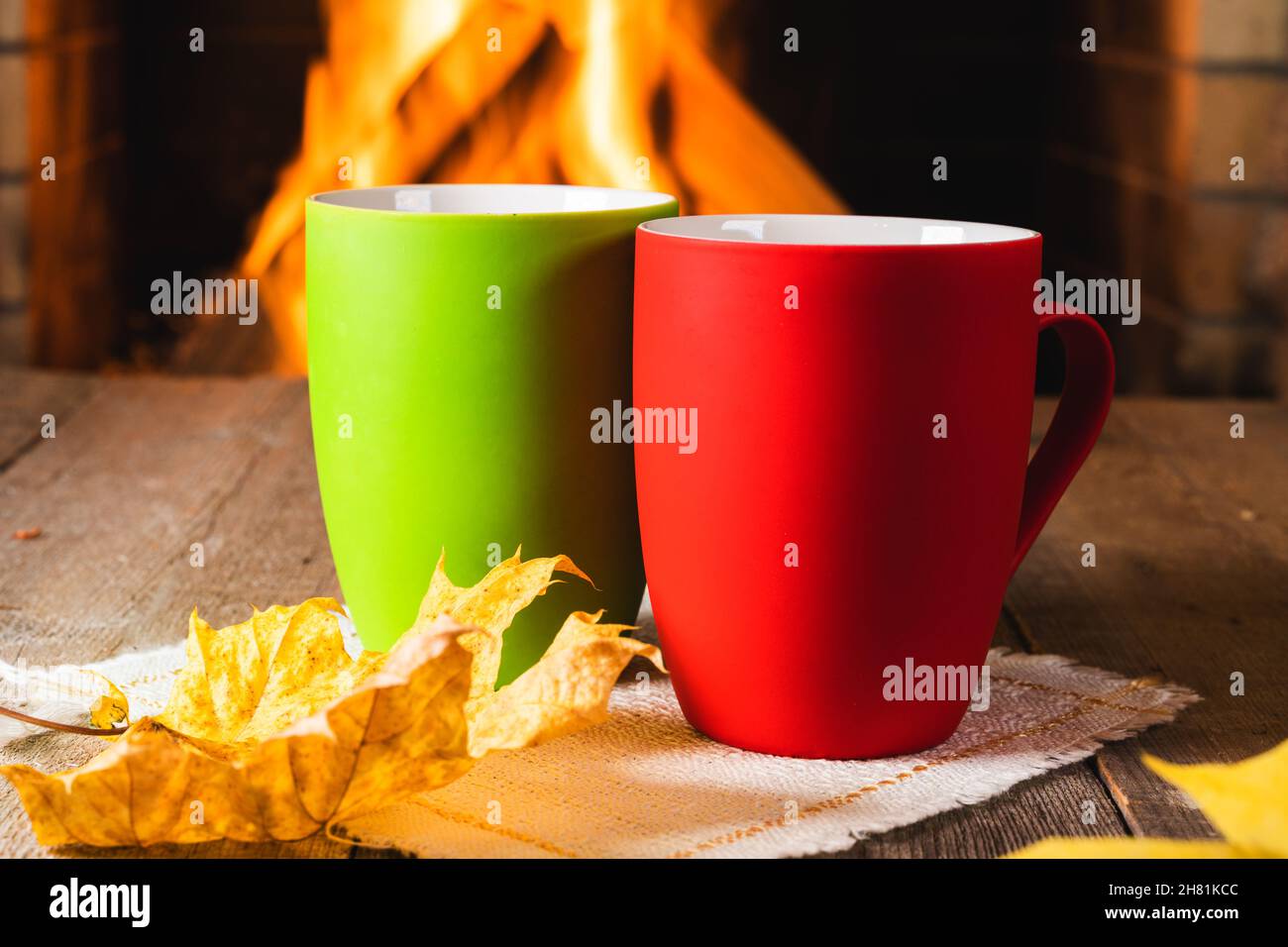Gemütliche Szene vor dem Kamin mit zwei Tassen Tee oder Kaffee und Herbstblättern. Stockfoto