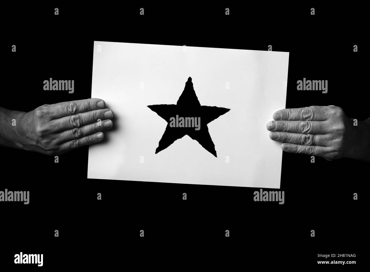 S+W-Bild mit männlichen Händen, die ein Blatt Papier mit einem weihnachts-Stern-Symbol auf schwarzem Hintergrund halten. Stockfoto