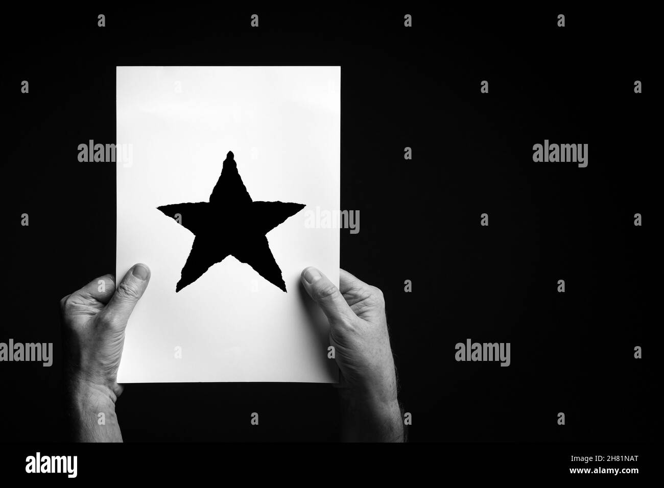 S+W-Bild mit männlichen Händen, die ein Blatt Papier mit einem weihnachts-Stern-Symbol auf schwarzem Hintergrund halten. Stockfoto
