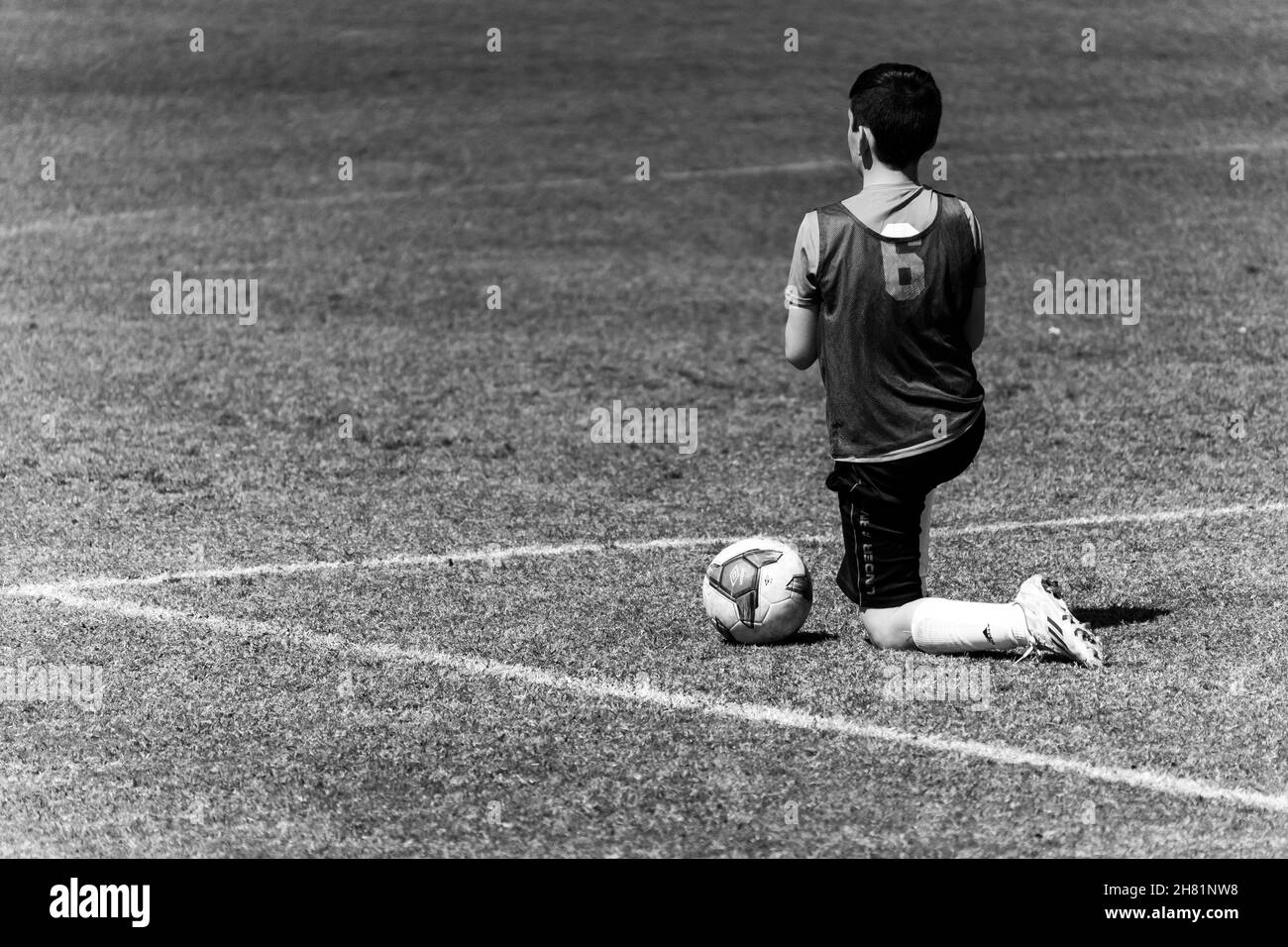 Graustufenaufnahme eines Fußballers der sechsten Nummer, der an einem sonnigen Tag in der Nähe des Balls auf dem Spielfeld kniet Stockfoto
