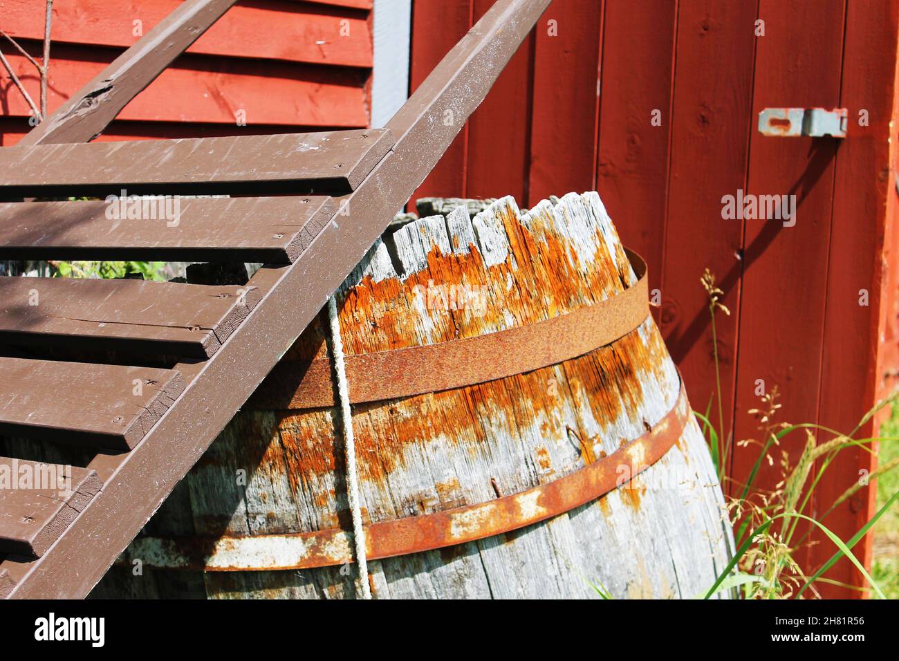 Nahaufnahme eines alten, verwitterten Holzfasses hinter einer Schranktür, unter den Griffen eines altmodischen hölzernen Handwagens. Stockfoto