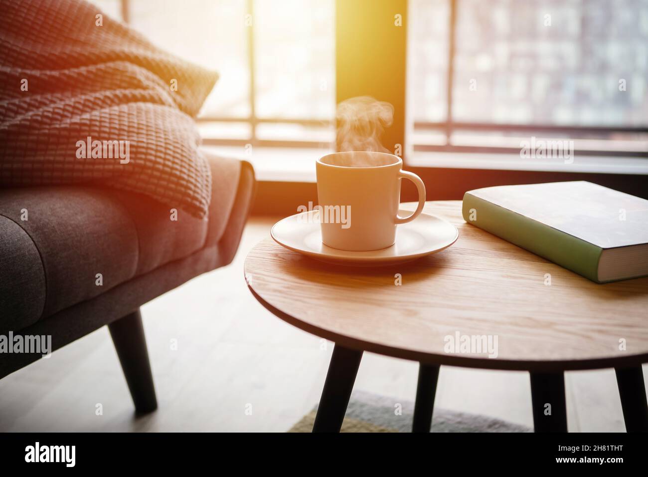 Entspannen Sie sich zu Hause bei einer Tasse heißen Tee und buchen Sie auf dem Couchtisch am Sofa Stockfoto