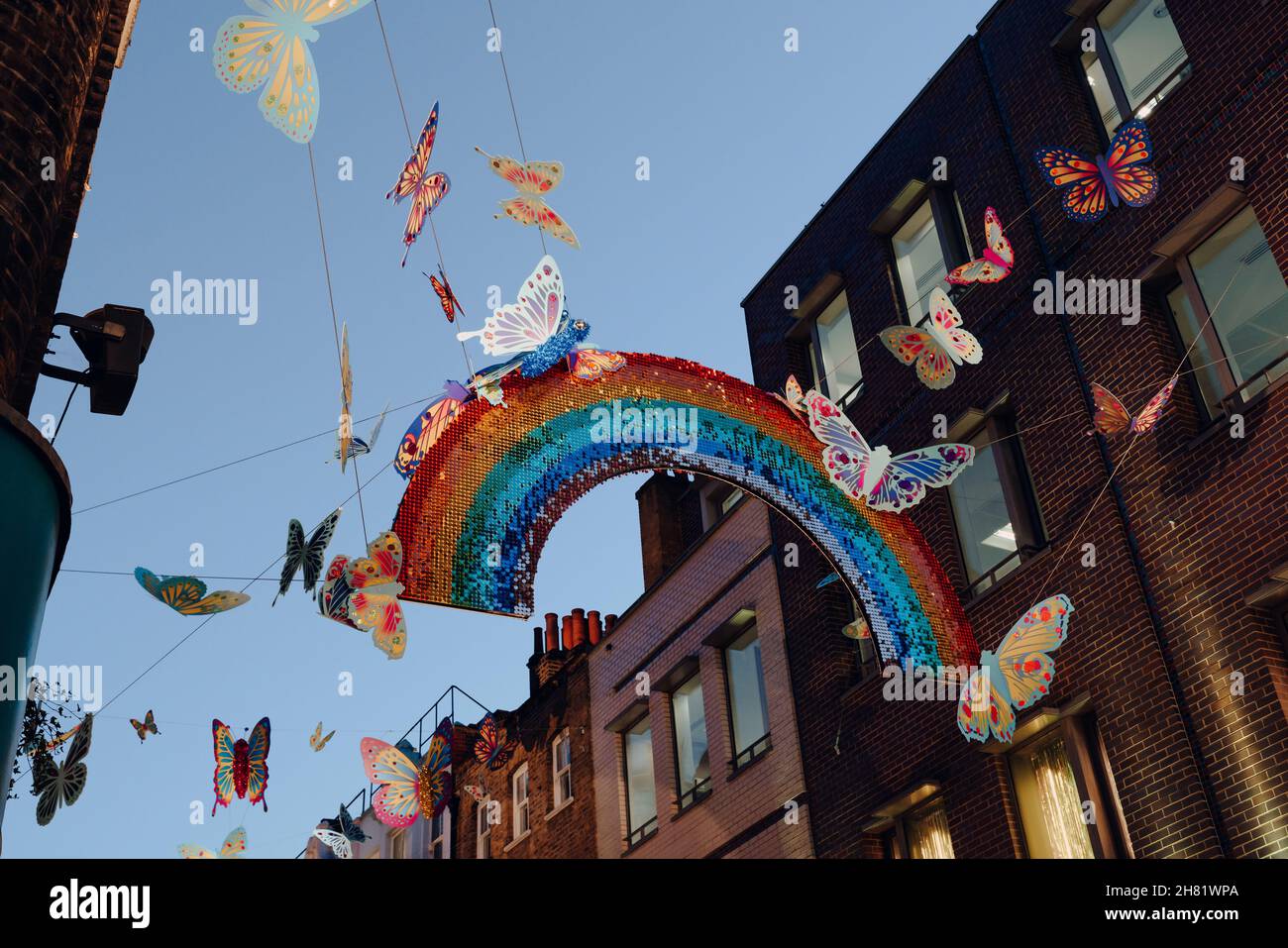 London, Großbritannien - 23. November 2021: Schimmerndes hängendes Regenbogenschild umgeben von Schmetterlingen auf der Carnaby Street als Teil der Weihnachtsinstallation in col Stockfoto